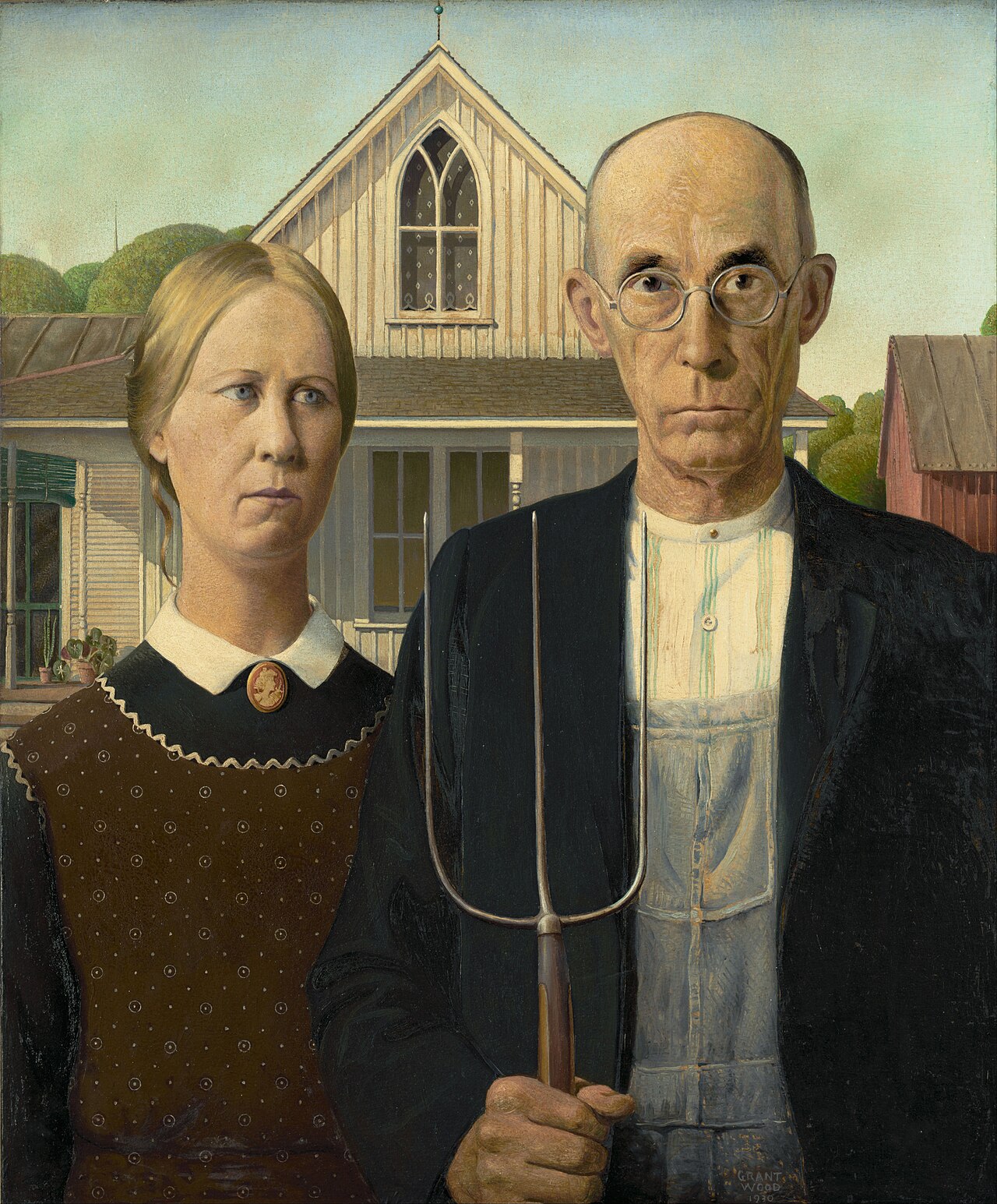 A realistic painting of two unsmiling people standing side by side. On the left is a woman with light brown hair pulled back, wearing a dark brown dotted dress, a white collar, and a cameo brooch; she looks slightly off to the side. On the right is a balding man with round glasses, wearing a black jacket over denim overalls and a buttoned white shirt; he faces forward and holds a three-pronged pitchfork. Behind them is a white wooden house with a pointed Gothic-style window, green trees, a red barn to the right, and a pale blue sky. The painting is signed Grant Wood 1930.