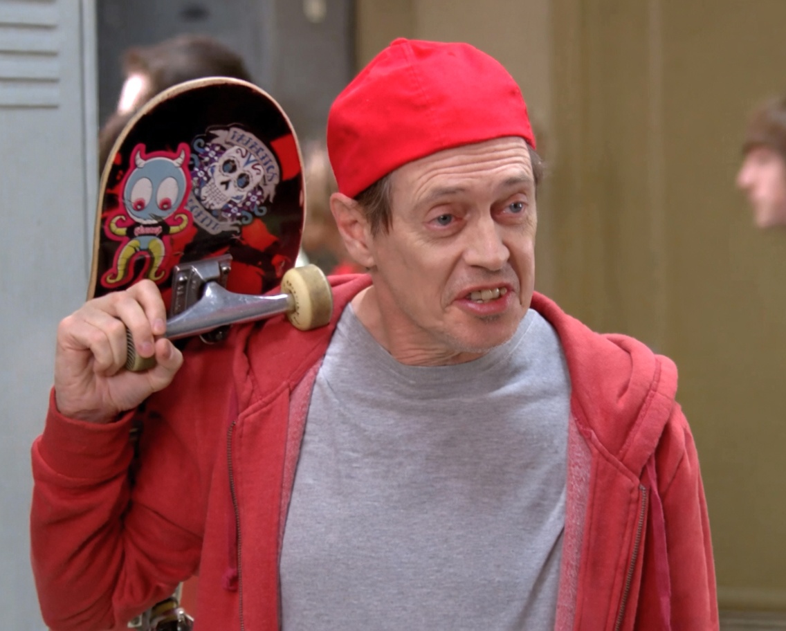 A middle-aged man with a strained, awkward smile wears a bright red beanie and a red zip-up hoodie over a gray t-shirt. He holds a colorful skateboard over one shoulder. The setting looks like a school hallway with lockers and blurred people in the background.