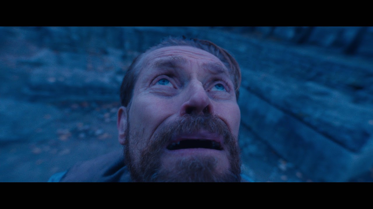 A letterboxed close-up of a bearded man with wide pale eyes and a slightly open mouth, staring sharply upward. Cool blue light covers his face. Behind him is a blurred, rocky surface. Thick black bars run across the top and bottom of the frame.
